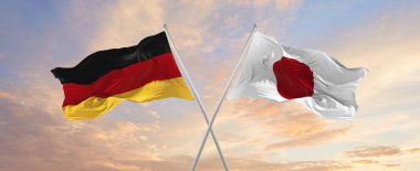flags of Germany and japan waving in the wind on flagpoles against sky with clouds on sunny day. Symbolizing relationship, dialog between two countries. 3d illustration,