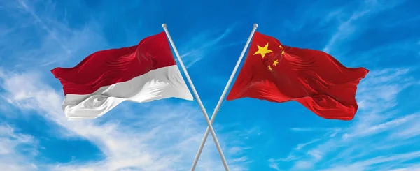 flags of China and Indonesia waving in the wind on flagpoles against sky with clouds on sunny day. Symbolizing relationship, dialog between two countries. 3d illustration,