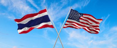 flags of USA and thailand waving in the wind on flagpoles against the sky with clouds on sunny day. Symbolizing relationship, dialog between two countries. 3d illustration,