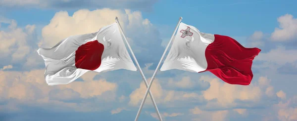 晴れた日には日本とマルタの旗が旗竿に風になびいて空に向かって雲を振っています 関係を象徴し 両国間の対話 3Dイラスト — ストック写真