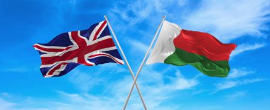 Büyük Britanya ve Madagaskar 'ın bayrakları güneşli bir günde gökyüzüne karşı bayrak direkleri üzerinde rüzgarda sallanıyor. İki ülke arasındaki ilişkiyi, diyaloğu sembolize ediyor. 3d illüstrasyon,