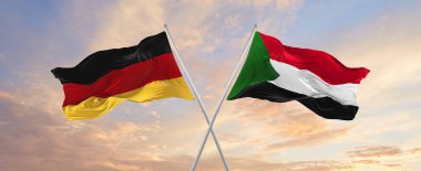 Almanya ve Sudan 'ın bayrakları rüzgarda dalgalanırken bayrak direkleri gökyüzüne karşı güneşli bir günde. İki ülke arasındaki ilişkiyi, diyaloğu sembolize ediyor. 3d illüstrasyon,