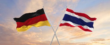 Almanya ve Tayland bayrakları rüzgarda dalgalanırken bayrak direkleri gökyüzüne karşı güneşli bir günde. İki ülke arasındaki ilişkiyi, diyaloğu sembolize ediyor. 3d illüstrasyon,