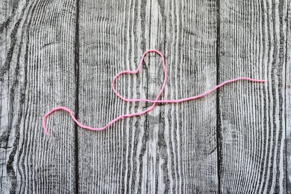 A pink wool heart on the grey wooden background.