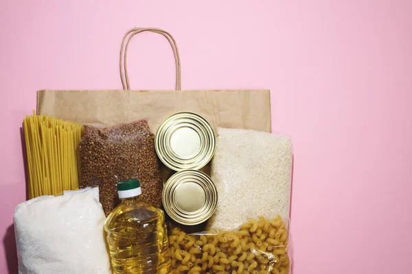 Food products for delivery. Flat lay donation food on craft paper bag on the pink background. Coronavirus donation food. Space for text. Top view.