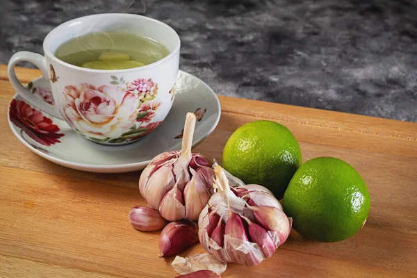 Lemon tea with garlic. Purple garlic and lemon, used in natural medicine. Cup with lemon tea and garlic on wood base. Garlic and lemon bulb. Image with space for texts.