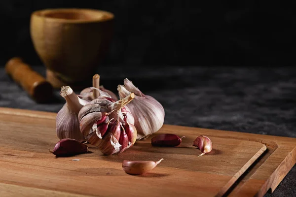 Garlic. Garlic clove, garlic bulb on wood base. Background with wooden pestle. Space for text on a dark background. Healthy food concept.