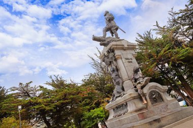 Beyaz bulutlarla kaplı mavi gökyüzüne karşı, yeşil bitki örtüsüyle çevrili, Punta Arenas, Şili 'deki Ferdinand Macellan anıtı..