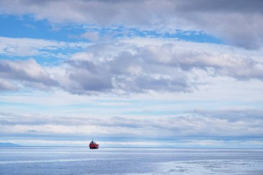 Punta Arenas yakınlarında okyanusta yüzen kargo gemisinin panoramik görüntüsü beyaz bulutlarla kaplı mavi gökyüzüne karşı..