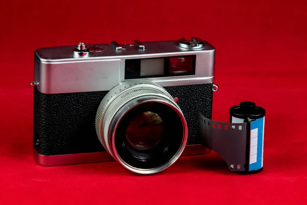 Vintage rangefinder film camera with roll of film on a red background