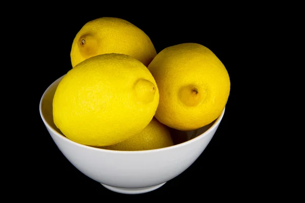 Limões inteiros na tigela branca em fundo preto — Fotografia de Stock