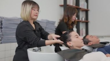 Profesyonel bir güzellik salonu çalışanı müşteri saçını suyla yıkıyor. Şampuanla temizle ve saçına saç kremiyle masaj yap. Güzellik salonu, saç bakımı ve kaplıca konsepti.