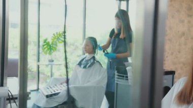 Kamera aynanın içinde hareket ediyor. Görüntülerde bir güzellik uzmanının kadın müşterinin saçını boyadığı ve saçını kesmek için makas ve tarak kullanan bir erkek berbere dönüştüğü görülüyor..