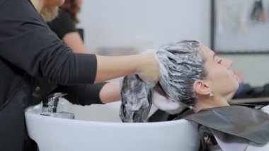 Profesyonel bir güzellik salonu çalışanı saçını yıkıyor. Şampuanla temizle ve saçına saç kremiyle masaj yap. Güzellik salonu, saç bakımı ve insan konsepti.