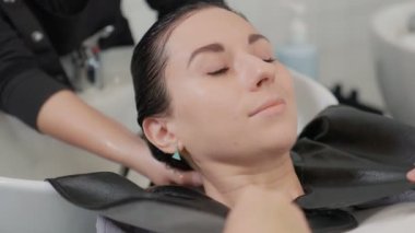 Beyaz, beyaz bir kadın kuaföre uzanıp berber dükkanında kuaförden saç yıkatıyor. Kuaför kuaförde saçlarını sıcak suyla yıkarken müşteriler rahatlıyor..