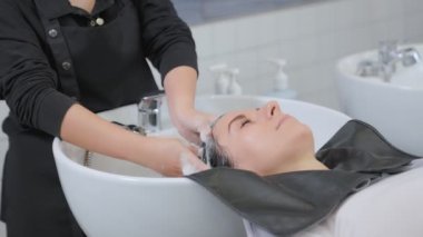 Profesyonel güzellik salonu çalışanları şampuanı suyla yıkıyor ve kızın saçına masaj yapıyor. Güzellik salonu, saç bakımı ve insan konsepti. Yavaş çekim.