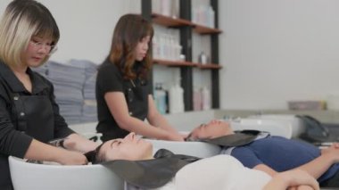 Profesyonel bir güzellik salonu çalışanı müşteri saçını suyla yıkıyor. Şampuanla temizle ve saçına saç kremiyle masaj yap. Güzellik salonu, saç bakımı ve berber konsepti..