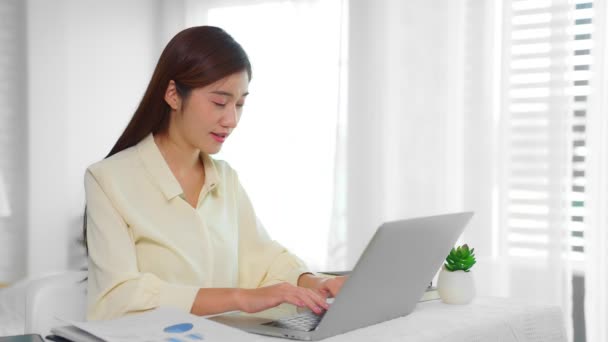 ノートPcのキーボードでメッセージを入力して仕事に座っている美しい女性は 喜んで笑顔 コロナウイルスの流行の仕事形態の家 — ストック動画