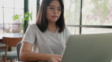 Genç iş kadınının bir kafede oturup dizüstü bilgisayarda çalışırken orta ölçekli bir fotoğrafı. İnternette çalışarak ya da çalışarak. Sokak kafesinde karışık ırk serbest çalışanı kadın.