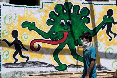 MUMBAI/INDIA - APRIL 26, 2020: A man wearing a face mask walks past a COVID-19 graffiti during the government-imposed nationwide lockdown as a preventive measure against the COVID-19 coronavirus.