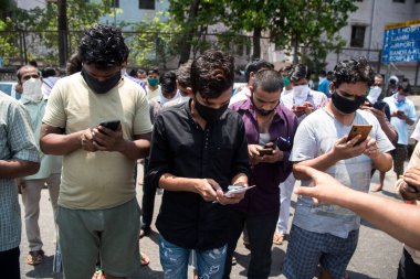 MUMBAI / INDIA - 2 Mayıs 2020: Göçmen işçiler COVID-19 Coronavirus 'a karşı önleyici bir önlem olarak ülke çapındaki tecrit süresince evlerine dönmek için kayıt olurken cep telefonlarına bakıyorlar.