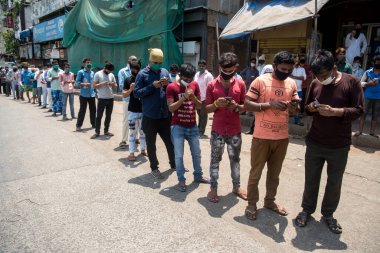 MUMBAI / INDIA - 2 Mayıs 2020: Göçmen işçiler COVID-19 Coronavirus 'a karşı önleyici bir önlem olarak ülke çapındaki tecrit süresince evlerine dönmek için kayıt olurken cep telefonlarına bakıyorlar.