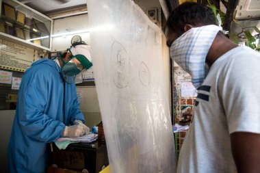 MUMBAI / INDIA - 7 Mayıs 2020: Koruyucu giysi giyen bir doktor, Dharavi gecekondu mahallesindeki bir klinikteki hastayı kontrol ediyor.