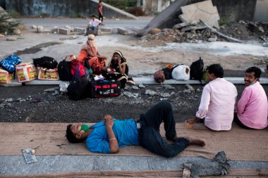 MUMBAI / INDIA - 9 Mayıs 2020: Göçmen işçiler, koronavirüsün yayılmasına karşı önleyici bir önlem olarak Bhiwandi otobanındaki eve dönüş yolculuklarında yolda oturuyorlar.