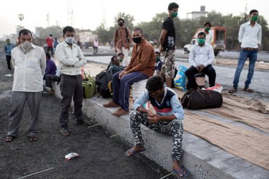 MUMBAI / INDIA - 9 Mayıs 2020: Göçmen işçiler, koronavirüsün yayılmasına karşı önleyici bir önlem olarak Bhiwandi otobanındaki eve dönüş yolculuklarında yolda oturuyorlar.