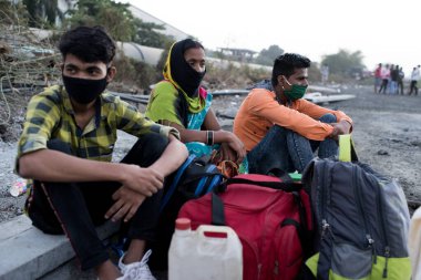 MUMBAI / INDIA - 9 Mayıs 2020: Göçmen işçiler, koronavirüsün yayılmasına karşı önleyici bir önlem olarak Bhiwandi otobanındaki eve dönüş yolculuklarında yolda oturuyorlar.
