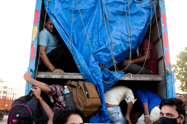 МУМБАЙ / ИНДИЯ - 9 мая 2020 года: Трудящиеся-мигранты забираются на грузовик со своим багажом по дороге домой на шоссе Бхиванди во время общенациональной изоляции в качестве профилактической меры против распространения коронавируса.