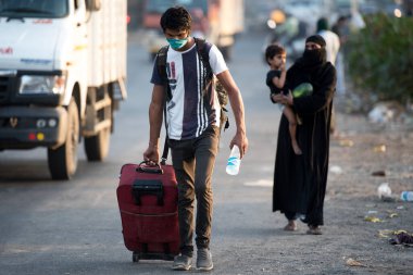 MUMBAI / INDIA - 11 Mayıs 2020: Coronavirus 'un yayılmasına karşı önleyici bir önlem olarak Bhiwandi karayolundaki yolculuklarında bavullarıyla yüz maskesi takan göçmen işçiler.