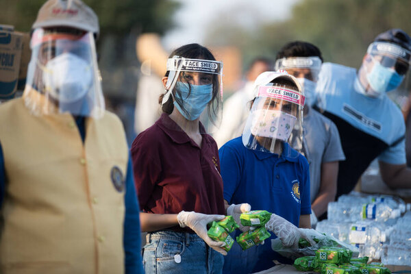 МУМБАЙ / ИНДИЯ - 11 мая 2020 года: Волонтеры в маске для лица распространяют воду среди рабочих-мигрантов на шоссе Бхиванди, которые возвращаются домой во время общенациональной изоляции в качестве превентивной меры против распространения коронавируса.