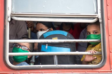 MUMBAI / INDIA - 16 Mayıs 2020: Yüz maskesi takan göçmen işçiler koronun yayılmasına karşı önleyici bir önlem olarak ülke çapındaki tecrit sırasında özel bir trene bindikleri için Lokmanya Tilak tren istasyonunda otobüste oturuyorlar