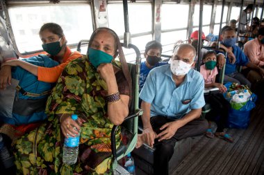 MUMBAI / INDIA - 16 Mayıs 2020: Yüz maskesi takan göçmen işçiler koronun yayılmasına karşı önleyici bir önlem olarak ülke çapındaki tecrit sırasında özel bir trene bindikleri için Lokmanya Tilak tren istasyonunda otobüste oturuyorlar