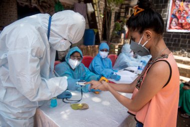 MUMBAI / INDIA - 10 Haziran 2020: Koruyucu giyimli bir tıbbi personel COVID test sürüşünde insanların nabzını ölçmek için bir oksimetre kullanır, Dharavi COVID-19 Coronavirus salgını sırasında