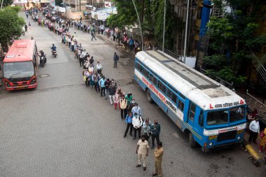 MUMBAI/INDIA- JUNE 15, 2020: Commuters wearing a facemask stand in queue wait to board a public transport bus in Dombivali. India has begun gradually lifting its restrictions imposed by the government.