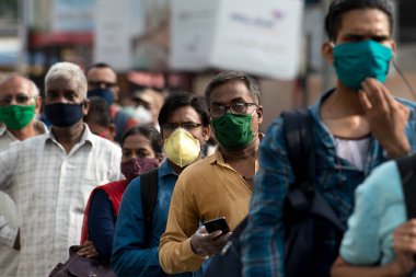 MUMBAI/INDIA- JUNE 15, 2020: Commuters wearing a facemask stand in queue wait to board a public transport bus in Dombivali. India has begun gradually lifting its restrictions imposed by the government.