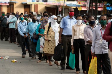 MUMBAI/INDIA- JUNE 15, 2020: Commuters wearing a facemask stand in queue wait to board a public transport bus in Dombivali. India has begun gradually lifting its restrictions imposed by the government.