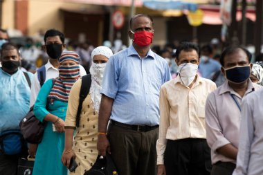 MUMBAI/INDIA- JUNE 15, 2020: Commuters wearing a facemask stand in queue wait to board a public transport bus in Dombivali. India has begun gradually lifting its restrictions imposed by the government.