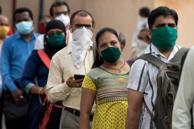MUMBAI/INDIA- JUNE 15, 2020: Commuters wearing a facemask stand in queue wait to board a public transport bus in Dombivali. India has begun gradually lifting its restrictions imposed by the government.