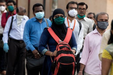 MUMBAI/INDIA- JUNE 15, 2020: Commuters wearing a facemask stand in queue wait to board a public transport bus in Dombivali. India has begun gradually lifting its restrictions imposed by the government.