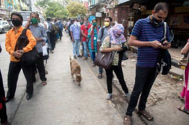 MUMBAI/INDIA- JUNE 15, 2020: Commuters wearing a facemask stand in queue wait to board a public transport bus in Dombivali. India has begun gradually lifting its restrictions imposed by the government.