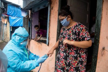 MUMBAI/INDIA- JUNE 17, 2020: Health workers wearing protective gear uses an oximeter to measure pulse of people at the COVID health check up camp at Ramabai colony slum during the COVID-19 Coronavirus pandemic.