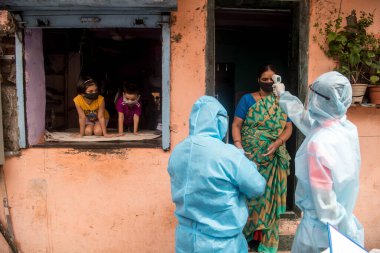 MUMBAI/INDIA- JUNE 17, 2020: Health workers wearing protective gear monitor body temperature of people at the COVID health check up camp at Ramabai colony slum during the COVID-19 Coronavirus pandemic.