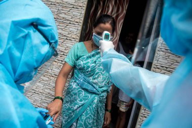 MUMBAI/INDIA- JUNE 17, 2020: Health workers wearing protective gear monitor body temperature of people at the COVID health check up camp at Ramabai colony slum during the COVID-19 Coronavirus pandemic.