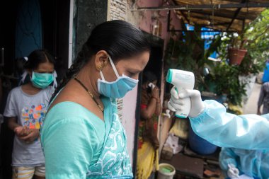 MUMBAI/INDIA- JUNE 17, 2020: Health workers wearing protective gear monitor body temperature of people at the COVID health check up camp at Ramabai colony slum during the COVID-19 Coronavirus pandemic.