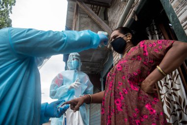 MUMBAI/INDIA- JUNE 17, 2020: Health workers wearing protective gear monitor body temperature of people at the COVID health check up camp at Ramabai colony slum during the COVID-19 Coronavirus pandemic.