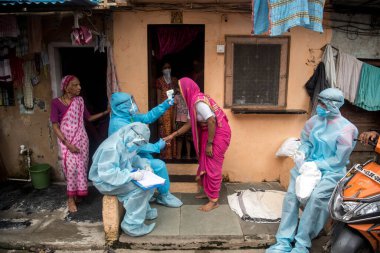 MUMBAI/INDIA- JUNE 17, 2020: Health workers wearing protective gear monitor body temperature of people at the COVID health check up camp at Ramabai colony slum during the COVID-19 Coronavirus pandemic.