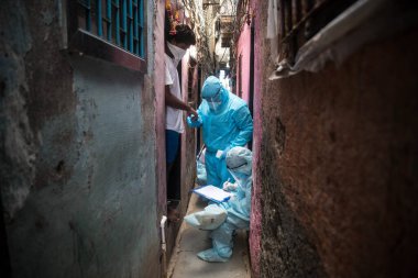 MUMBAI/INDIA- JUNE 17, 2020: Health workers wearing protective gear monitor body temperature of people at the COVID health check up camp at Ramabai colony slum during the COVID-19 Coronavirus pandemic.